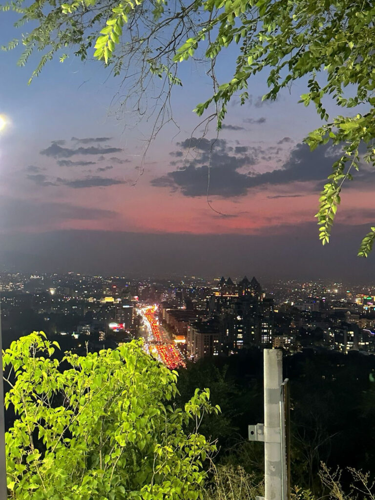 Panoramic view of Almaty city at sunset from Kok-Tobe Hill with traffic lights and buildings visible below.