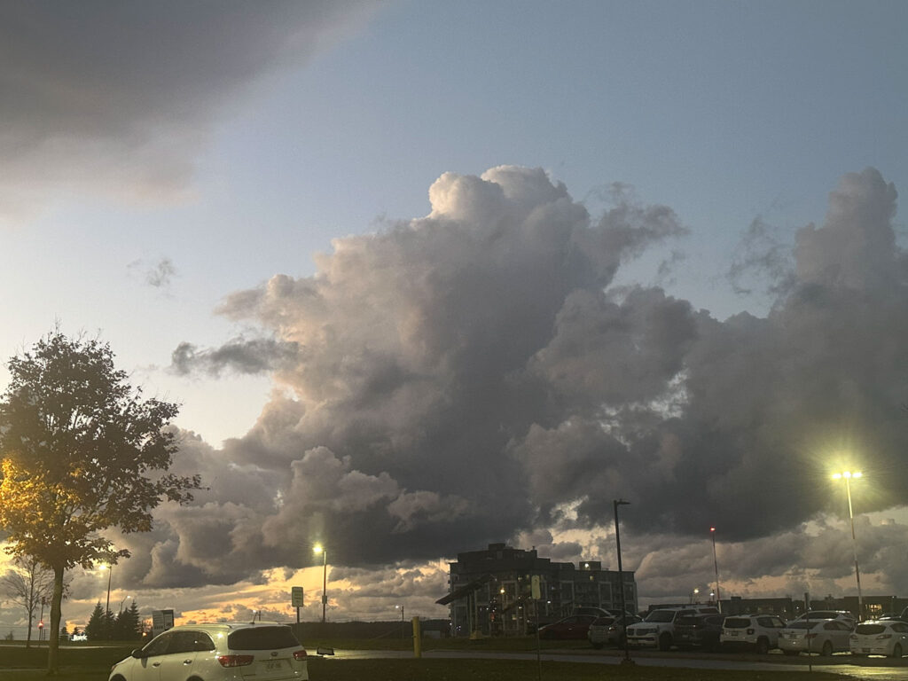 Large dark storm clouds forming over a parking lot during sunset with street lights and cars.